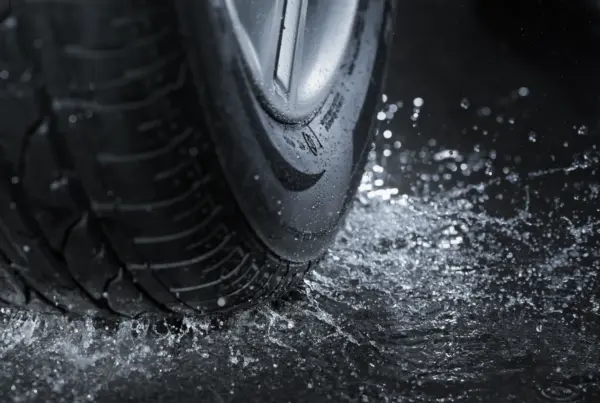 Close-up of a car tire and alloy wheel splashing through water on wet pavement.